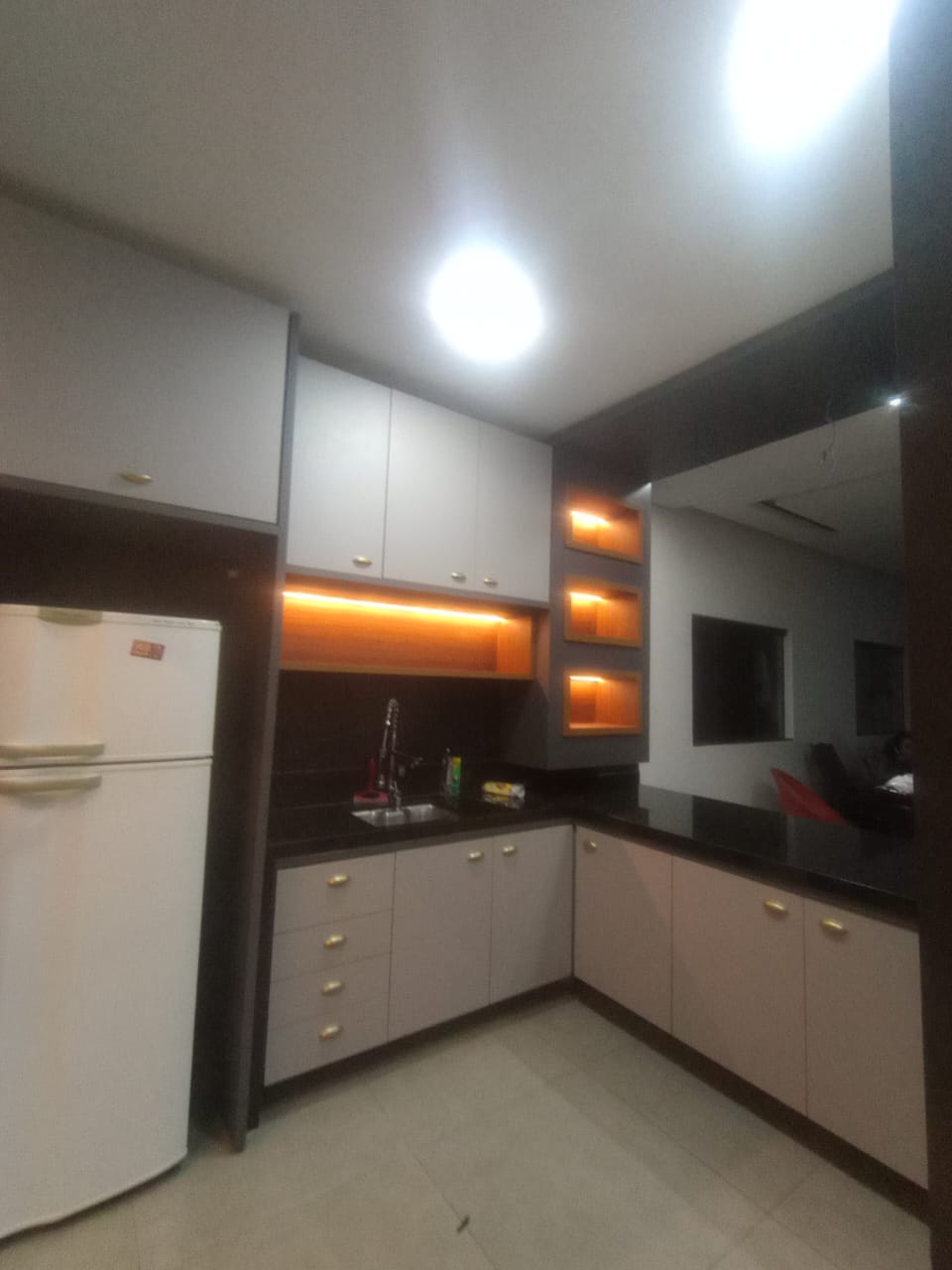 cozinha planejada cinza com bancada escura, iluminação em LED âmbar sob os armários e nichos iluminados