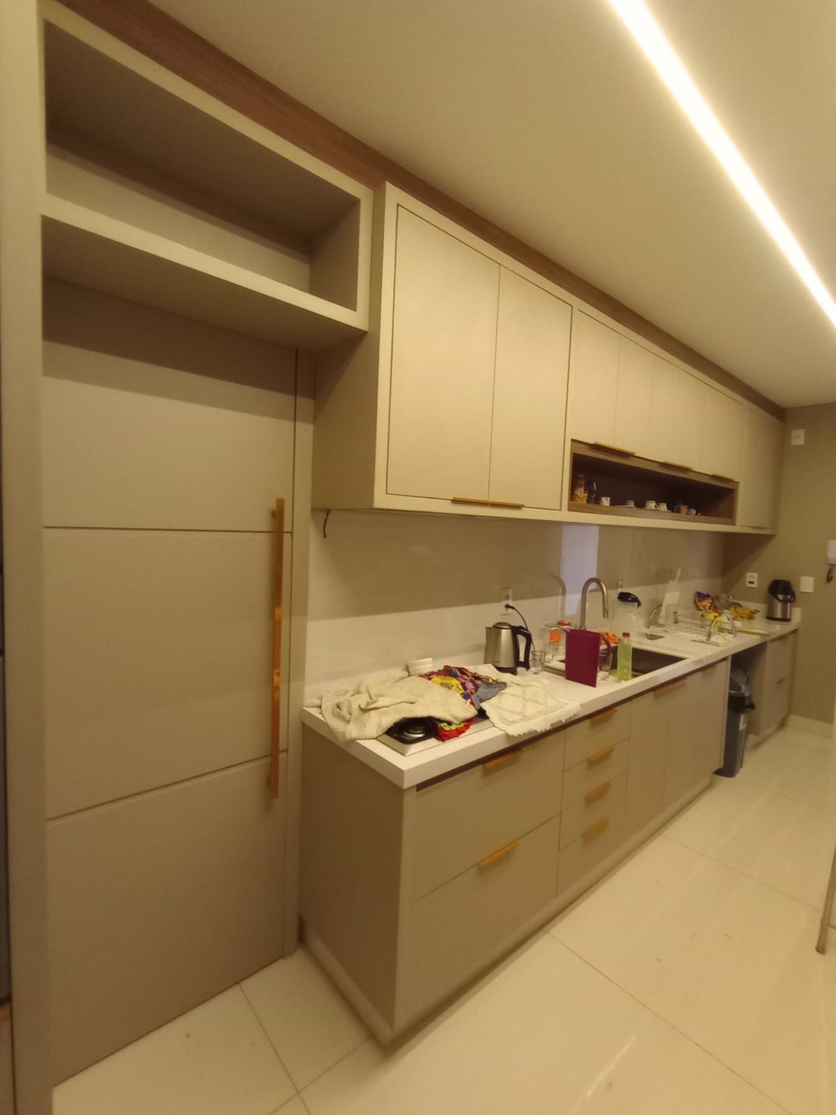 cozinha planejada bege com armários, bancada branca, lighting de LED no forro e geladeira embutida