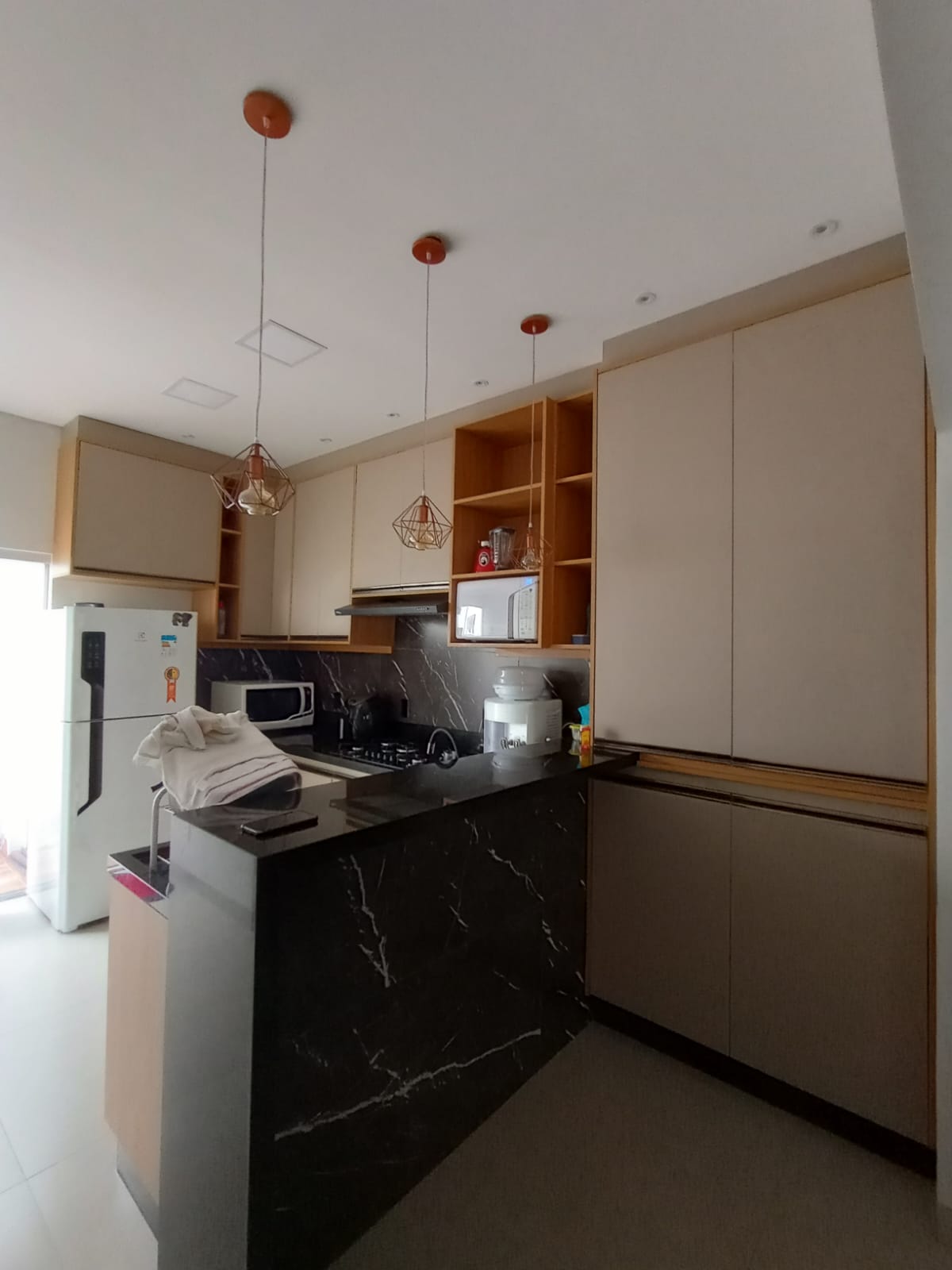 cozinha planejada com armários claros em madeira e off-white, bancada de mármore preto, pendentes dourados e e